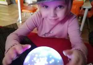 dziewczynka w brokatowym kapeluszu przy świecącej, kolorowej kuli.