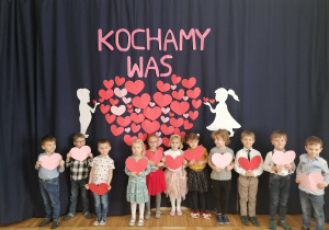 Grupa dzieci trzymająca serca na tle dekoracji z okazji Dnia Babci i Dziadka