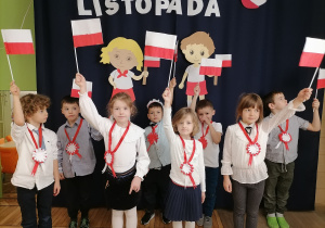 Grupa dzieci ubranych na galowo machająca flagami Polski.