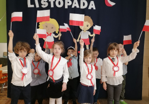 Grupa dzieci ubranych na galowo machająca flagami Polski.