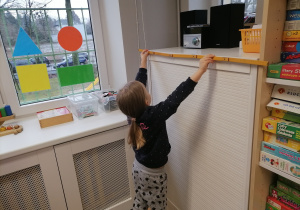 Dziewczynka mierząca linijką szerokość szafki.