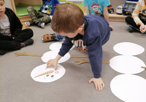 Chłopiec układający elementy bałwana na dywanie.