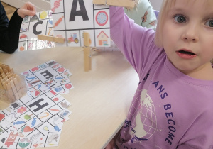 Dziewczynka pokazująca zaznaczone na kartce obrazki, których nazwy zaczynają się na literę A.