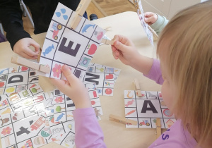 Dziewczynka zaznaczająca na karcie obrazki pasujące do danej litery.