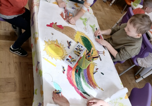 Czworo dzieci koloruje obrazek koguta.