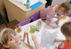Troje dzieci koloruje obrazek króliczka.