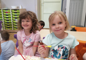 Dziewczynki uśmiechnięte pozują do zdjęcia podczas malowania ramek.