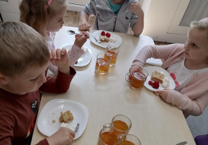 Dzieci wspólnie jedzą śniadanie w postaci szarlotki z truskawkami.