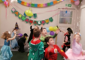 Dzieci przebrane za różnych bohaterów tańczą w sali.