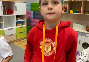 Chłopiec w papierowej koronie z medalem Super Chłopaka na szyji.