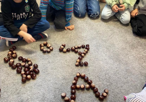 Dzieci układają literę "A" z kasztanów