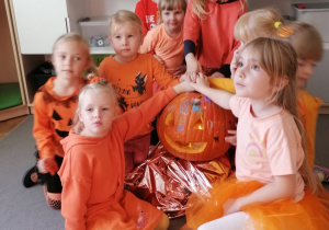 Grupa dziewczynek ubranych na pomarańczowo wraz z dynią