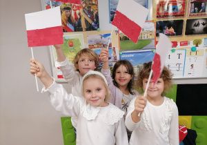 Trzy dziewczynki i jeden chłopiec trzymają w rękach własnoręcznie wykonane flagi Polski