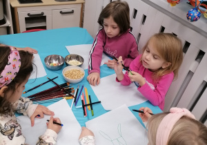 Pięć dziewczynek przy stoliku, które projektują obraz z czekolady.