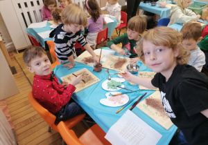 Grupa chłopców przy stolikach maluje czekolada po waflach.