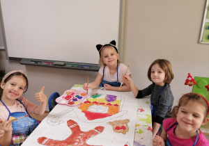 Grupa dziewczynek maluje przy stoliku farbami domek z piernika oraz pierniczka świątecznego.