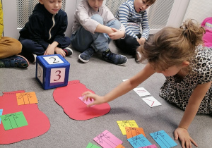 Dzieci grają w grę, rzucając kostką i wkładając odpowiednią liczbę prezentów do worka.