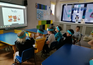 Dzieci w zimowych opaskach oglądają prezentację na temat zimy.