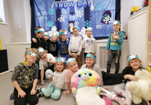 Grupa dzieci wraz z zimowymi maskotkami pozuje do zdjęcia na tle zimowej dekoracji.