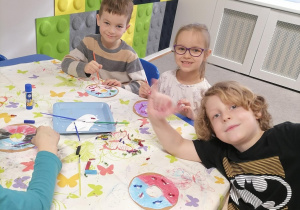 Dzieci przy stolikach malują oraz ozdabiają papierowe pączki.