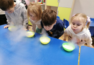 Czworo dzieci dmucha w miseczki z suchym lodem tworząc małe chmurki.