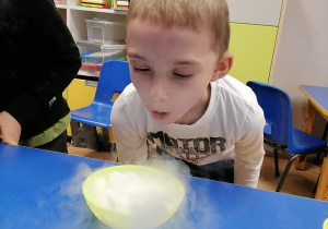Chłopiec dmucha w miseczkę z suchym lodem, tworząc małą chmurkę.