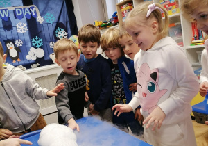 Dzieci przy stoliku obserwują suchy lód w miseczkach.