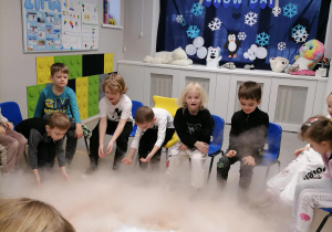 Dzieci siedząc w kole obserwują zjawisko dymu z suchego lodu.