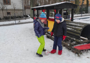 Dwóch chłopców gra w piłkę na śniegu.