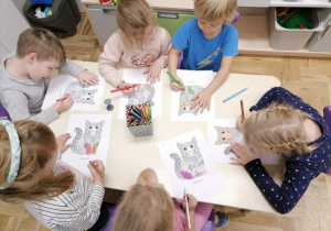 Dzieci siedzące przy stoliku kolorujące mandale - koty.