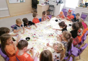 Dzieci siedzące przy stoliku i ozdabiające małe dynie.