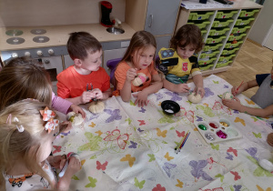 Dzieci siedzące przy stoliku i ozdabiające małe dynie.