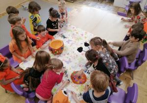 Dzieci siedzące przy stoliku i ozdabiające dużą dynię.