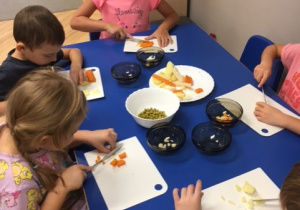 Dzieci krojące warzywa przy stoliku.