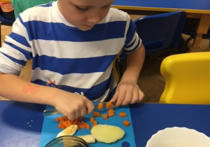 Chłopiec krojący warzywa przy stoliku.