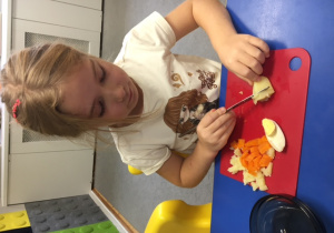 Dziewczynka krojąca warzywa przy stoliku.