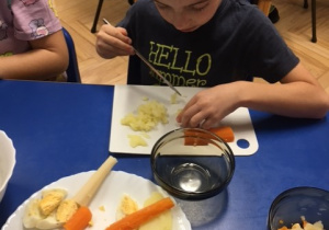 Chłopiec krojący warzywa przy stoliku.