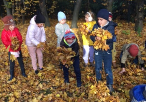 Grupa dzieci bawiąca się jesiennymi liśćmi.