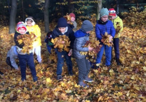 Grupa dzieci bawiąca się jesiennymi liśćmi.