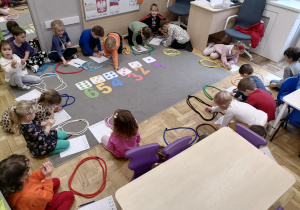 Grupa dzieci siedząca na dywanie i rzucająca kośćmi do gry.
