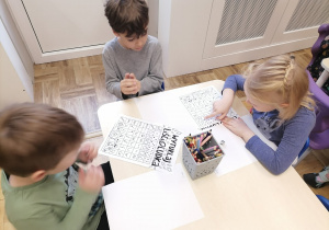 Grupa dzieci siedząca przy stoliku i rzucająca kośćmi do gry rysując liścioludka.