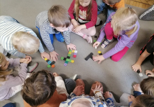 Dzieci siedzące na dywanie i układające literę T z klocków.
