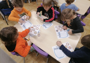 Dzieci siedzące przy stoliku i wycinające obrazki z głoską T.