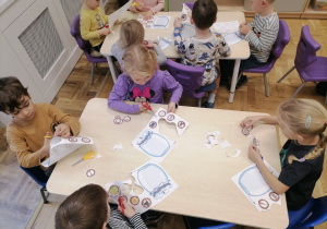 Dzieci siedzące przy stoliku i wycinające obrazki z głoską T.