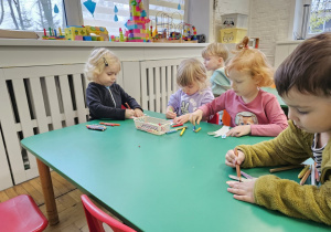 Dzieci siedzące przy stoliku wykonujące pracę plastyczną.
