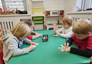 Dzieci siedzące przy stoliku wykonujące pracę plastyczną.