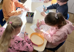 Grupa dzieci siedząca przy stoliku kolorująca pracę.