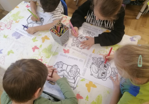 Dzieci siedzące przy stoliku kolorujące pracę.