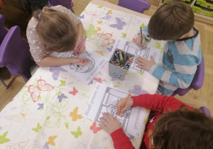 Dzieci siedzące przy stoliku kolorujące pracę.