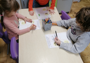 Dzieci wykonujące pracę plastyczną przy stoliku.